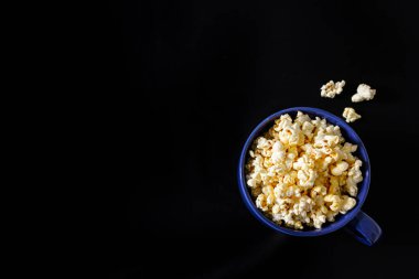 Siyah arka planda patlamış mısırla dolu mavi bardağın üst görüntüsü