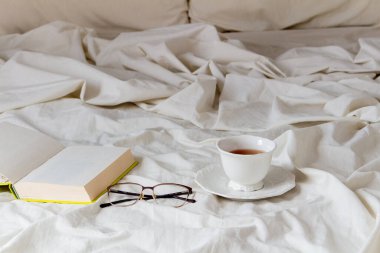 Bardaklı açık kitap ve çarşafta bir fincan çay.