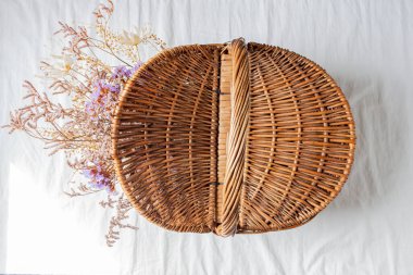 Beyaz pamuk kumaş arka planında kurumuş çiçeklerle dolu bir piknik sepeti. Düz yatıyordu. Piknik konsepti. 