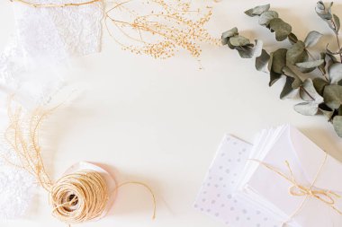 Bej rengi düğün davetiyeleri kompozisyonu. Beyaz zarflar, kurumuş çiçekler, dantel kumaş, beyaz arka planda sisal ip. Düz yerde, üst tarafta. Nötr durağan. 