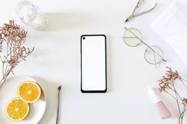 Sağlık hizmeti spa konsepti. Kurumuş çiçekler, bardaklar, cep telefonları, portakal dilimleri, tırnak makasları, havlular ve beyaz arka planda banyo tuzu. Düz yerde, üst tarafta. Güzellik, cilt bakımı, kompozisyon.