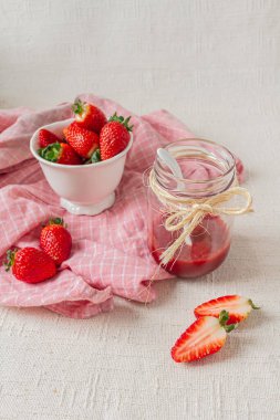 Kavanozda çilek reçeli, içinde küçük beyaz bir kaşık ve kasede taze çilek. Hafif arkaplan. Mevsimlik yeme konsepti. 