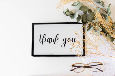 Ekrandaki teşekkür cümlesi ve beyaz arkaplanda kurumuş çiçekleri içeren dijital tabletin üst görünümü