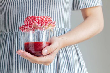 Bir kavanoz çilek reçeli tutan genç bir kadın..