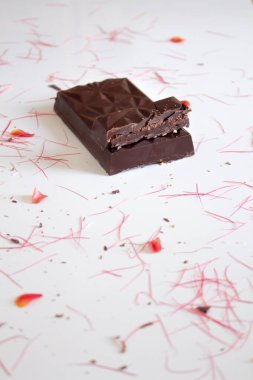 Etrafında çiçek yaprakları olan beyaz arkaplanda siyah çikolata görüntüsü