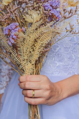 Güzel gelinin kurumuş çiçeklerle buketi tutarken çekilmiş bir fotoğrafı.