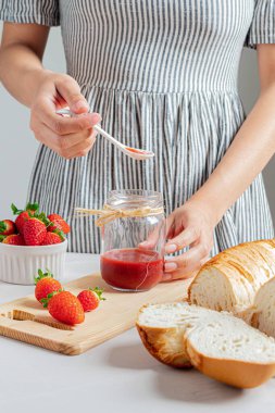 Bir kavanoz çilek reçeli tutan genç bir kadın..