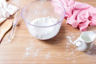 Hamuru hazırlama süreci. Kâsede un, yumurta, mutfak örtüsü ve mutfak gereçleri ahşap masada.