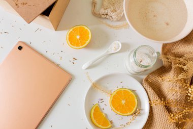 Tahta kutulu bej bej bej kompozisyonu, su dolu kâse, portakal dilimleri, boş ekran tableti ve beyaz arka planda banyo tuzu. Düz yerde, üst tarafta. Kadın güzellik tedavi rutin konsepti. 