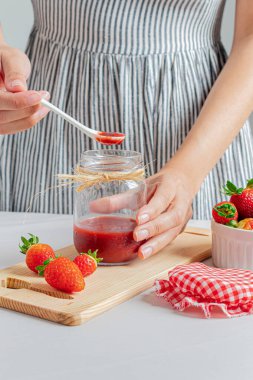 Bir kavanoz çilek reçeli tutan genç bir kadın..