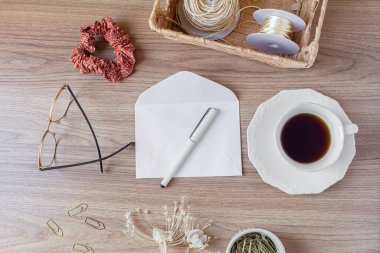 Tahta masadaki zarf. Ofis masası çalışma alanı, yabani çiçekler, bir fincan kahve, saç tokası ve kırtasiye malzemeleri. Düz yerde, üst tarafta. Samimi kompozisyon. Romantik harf kavramı. 