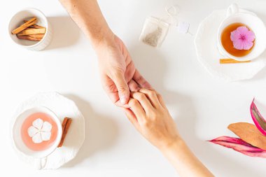 İki kişilik masa, içinde çiçek olan iki fincan çay, pembe ve kahverengi yapraklar, çay poşeti, beyaz arka planda tarçın. Düz yerde, üst tarafta. Boşluğu kopyala. 