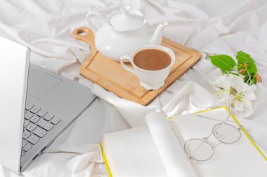 Dizüstü bilgisayar, kahve ve çiçekler yatakta.