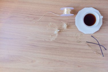 Bir fincan kahve, kalem, ataç, bardaklar, ip, kurumuş çiçekler ve tahta bir arka planda yapraklar. Düz yatış, üst görünüm. 