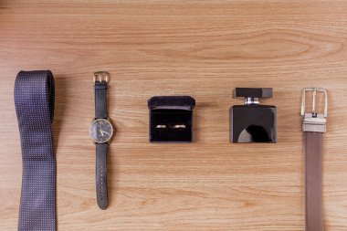 Erkek zarif aksesuarları. Kravatın üst görüntüsü, kol saati, altın yüzükler, parfüm ve kahverengi kemer ahşap bir arka planda. Moda konsepti. 