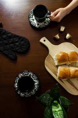 Dümdüz uzanmış, iki fincan kahvenin üst görüntüsü, tahta tahtada bitki ve ekmek çörekleri, koyu ahşap masa. 