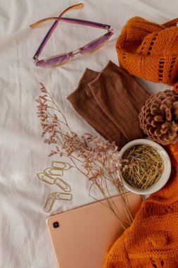 Autumn, sonbahar kompozisyonu. Kahverengi sıcak çorap ve süveterli bej keten yatak, altın ataç, altın tablet, okaliptüs yaprakları, bir fincan kahve ve bardak. Yaşam tarzı, moda mevsimi konsepti. 