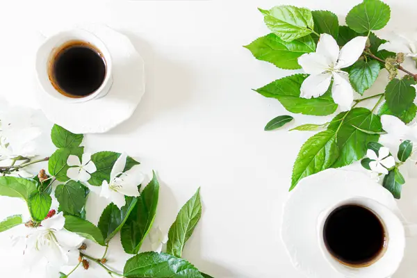 用白色花朵和绿色叶子装饰在白色背景上的杯子里的芳香的黑咖啡的顶部视图 — 图库照片