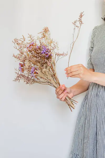 白い背景に乾いた花束を保持するストライプビンテージドレスの若い美しい女性 フローリスト ミニマルコンセプト — ストック写真
