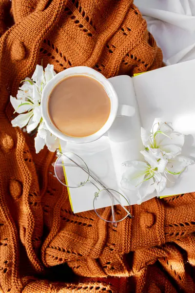 Slow morning composition. Book, coffee with milk, flowers, glasses on a messy bed. Fall, autumn concept.