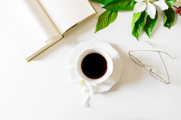 顶部的黑色咖啡杯 眼镜和打开的书装饰着白花和黑莓树叶子白色背景 春天的概念 — 图库照片