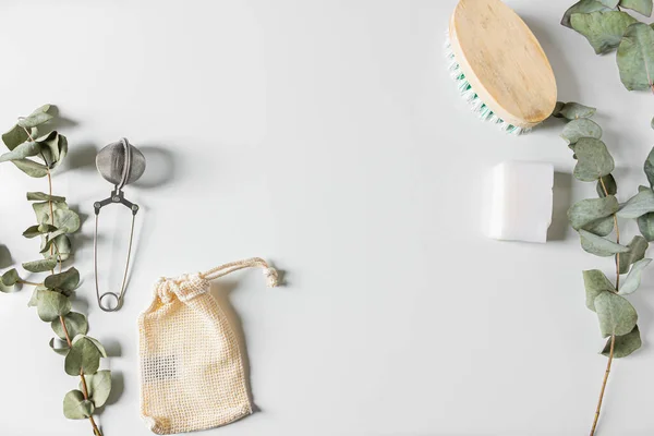 Beige eco style feminine household supplies: cleaning brush, cotton bag, tea strainer, coconut soap and eucalyptus leaves on white background. Flat lay, top view. Eco friendly minimalist concept.