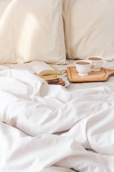 早上浪漫早餐的概念 新鲜的切片面包 一杯咖啡 床上有书 还有米色的薄片和枕头 — 图库照片