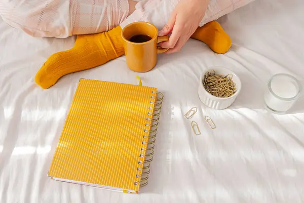 一个女人穿着睡衣 躺在床上喝咖啡 带着计划书 一些剪纸夹和瓦希带子 自由职业者 从家里工作 懒洋洋的一天 舒适的家的概念 — 图库照片