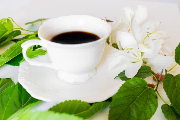 Nahaufnahme Einer Schwarzen Kaffeetasse Mit Weißen Blüten Und Grünen Blättern — Stockfoto
