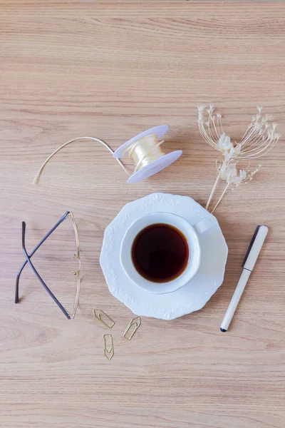 Cup of coffee, pen, paper clips, glasses, string and dried flowers on wooden background.