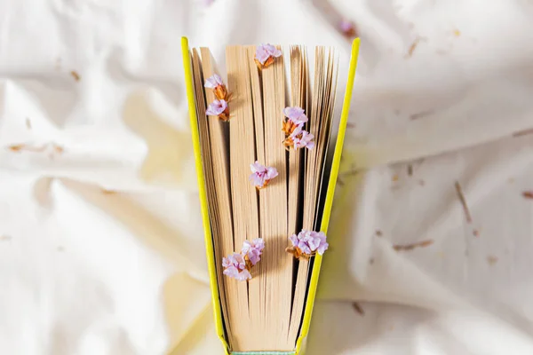 秋のコンポジション 白いベッドシートに書かれた本で ライラックの小さな花がページに差し込まれています フラットレイ トップビュー — ストック写真