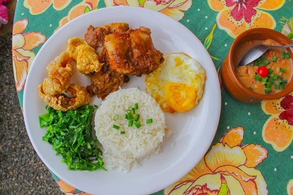 Typical Brazilian Dish from Minas Gerais with beans, pepper, fried egg, rice, crackling, chop and kale butter, all placed on a table with flowers design cloth - Food Styling