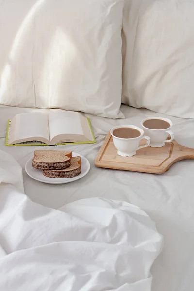 朝のロマンチックな朝食コンセプト ベッドで本とコーヒーのカップと新鮮なスライスしたパン — ストック写真
