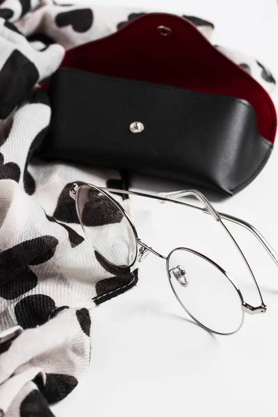 Eyeglasses, case and scarf on white background.