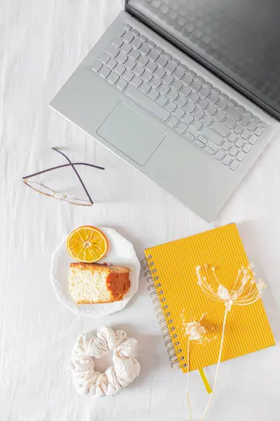 有笔记本电脑 橙子蛋糕 规划器 刮胡刀和白底干花的家庭办公台架 — 图库照片
