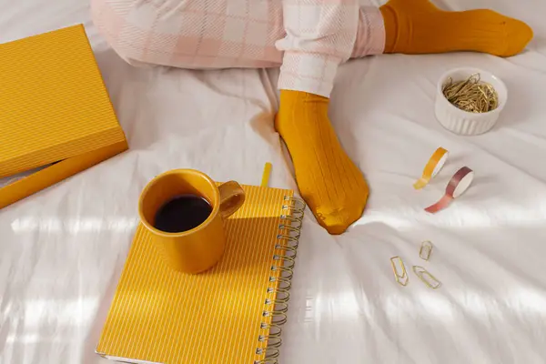 一个女人穿着睡衣 躺在床上喝咖啡 带着计划书 一些剪纸夹和瓦希带子 自由职业者 从家里工作 懒洋洋的一天 舒适的家的概念 — 图库照片