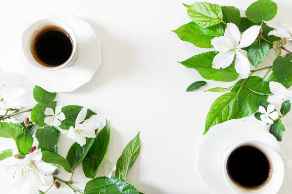 緑の葉と白い花で装飾されたブラックコーヒーの2カップのトップビュー — ストック写真
