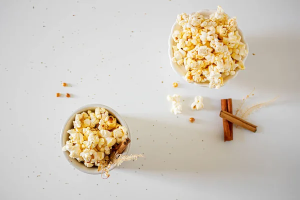 Top view of popcorn in bowls with cinnamon sticks on white background. Autumn, winter food concept.