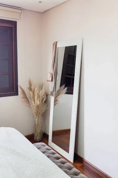 Stylish bedroom with mirror and bouquet of dried flowers. Modern classic design.