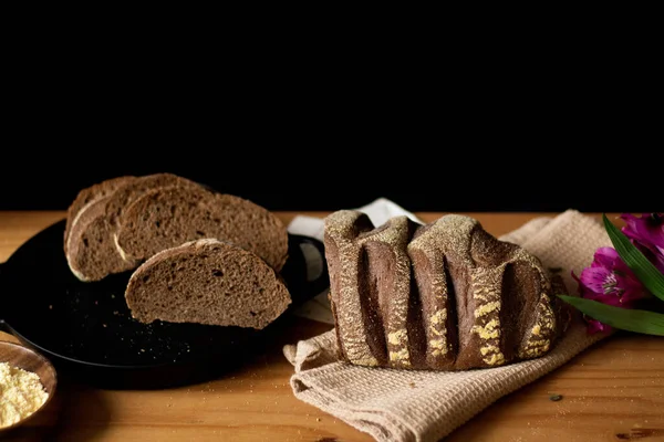 Celý Nakrájený Hnědý Chléb Dřevěný Stolek Zdobený Květinami Temné Složení — Stock fotografie