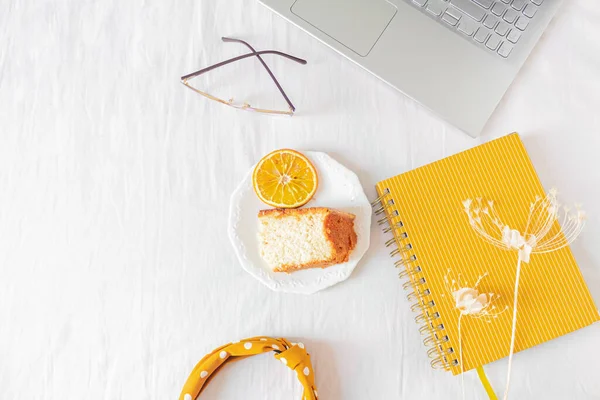 ホワイトバックのラップトップ オレンジ色のケーキ ヘッドバンド メガネ ベージュのワイルドフラワー ノートブック付きのホームオフィスデスクフレーム フラットレイ トップビュー 女性ビジネスコンセプト — ストック写真