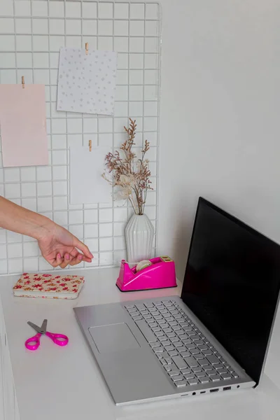 Aesthetic minimalist home office desk workspace Female hand using sticky tape near laptop on white desk.