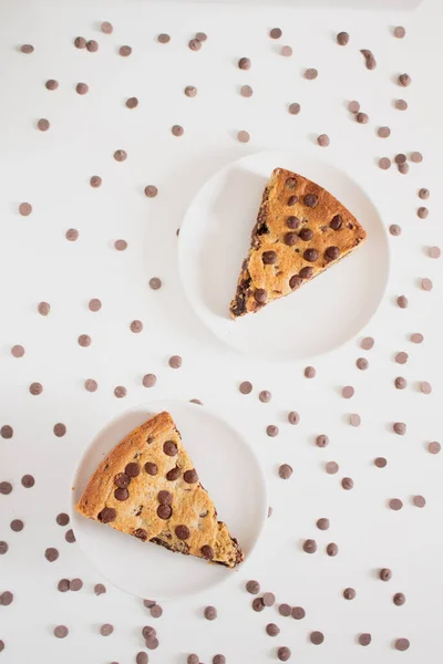 Top view of cookie pie slices in white plates with chocolate chips around on light background. Breakfast concept.