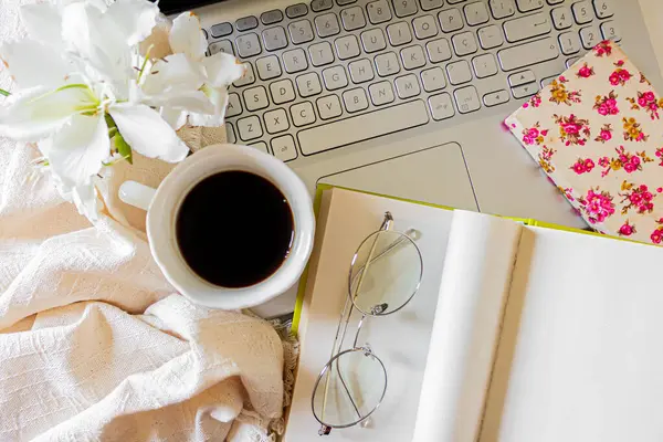 Laptop, notepad, book, glasses, linen fabric, cup of coffee and white flowers collage. Flat lay, top view. Aesthetic, minimal, home office workspace.