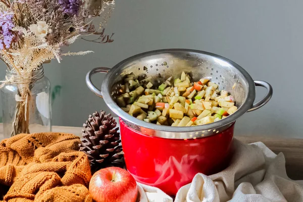 Sonbahar pastası konsepti. Dilimlenmiş elmalar kahverengi süveter ve ahşap masa üzerinde çam kozalağı ile metal kevgir.