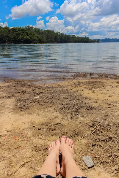 female legs on a sandy shore with a lake