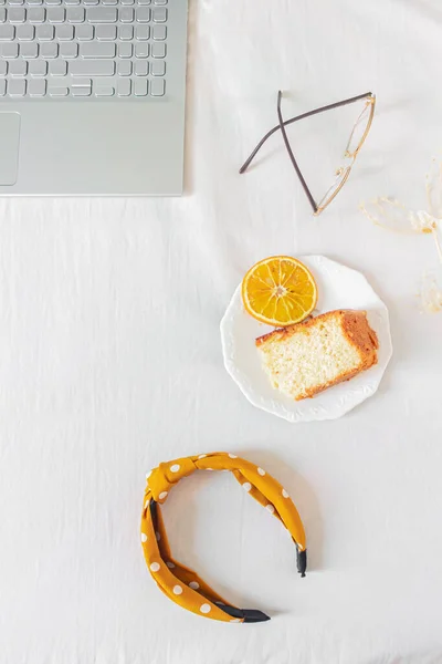 有笔记本电脑 橙色蛋糕 眼镜和白色背景的米黄色野花的家庭写字台框架 平躺在地上 尽收眼底 妇女的商业概念 — 图库照片