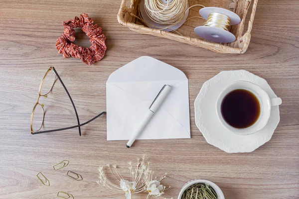 Tahta masadaki zarf. Ofis masası çalışma alanı, yabani çiçekler, bir fincan kahve, saç tokası ve kırtasiye malzemeleri. Düz yerde, üst tarafta. Samimi kompozisyon. Romantik harf kavramı. 