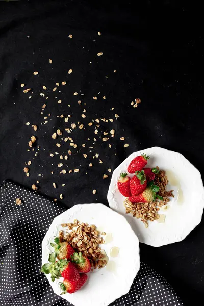 朝食のためのイチゴ 白いプレートと黒の背景にグラノーラと蜂蜜が付いているイチゴ — ストック写真