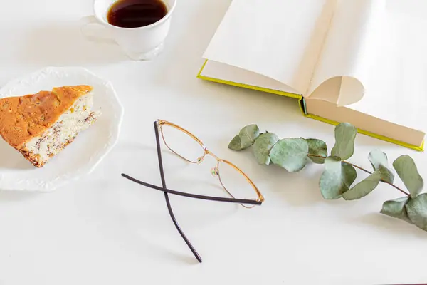 Breakfast composition with coffee, book, piece of cake and glasses on white background. Slow morning routine concept.